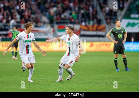 28. Oktober 2023, Bayern, Augsburg: Fußball: Bundesliga, FC Augsburg - VfL Wolfsburg, Spieltag 9, WWK Arena. Arne Engels (l) feiert mit Kapitän Ermedin Demirovic vom FC Augsburg nach dem Tor für Augsburg 2-2 sieht Yannick Gerhardt vom VfL Wolfsburg (r) enttäuscht aus. Foto: Daniel Löb/dpa - WICHTIGER HINWEIS: Gemäß den Vorgaben der DFL Deutsche Fußball Liga und des DFB Deutscher Fußball-Bund ist es verboten, im Stadion und/oder des Spiels aufgenommene Fotografien in Form von Sequenzbildern und/oder videoähnlichen Fotoserien zu verwenden oder verwenden zu lassen. Stockfoto