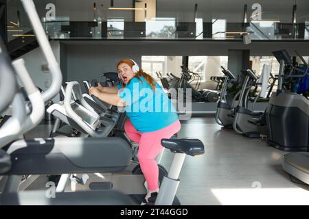 Eine verrückte motivierte übergewichtige Frau, die schnell auf dem Heimtrainer fährt Stockfoto