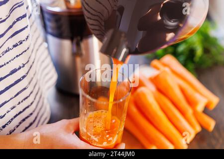 Eine Frau gießt frischen Karottensaft ins Glas. Frisch gepresster Karottensaft Stockfoto