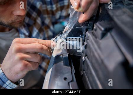 Zugeschnittener Nahaufnahme Mann, der in der Garage arbeitet und Schutzfolie auf dem Scheinwerfer aufträgt Stockfoto
