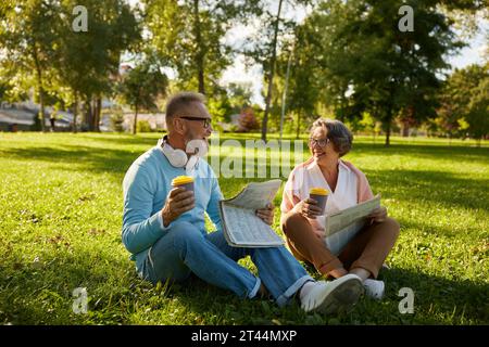 Seniorenliebende Paare, die sich im Park im Freien entspannen und Zeitung lesen Stockfoto