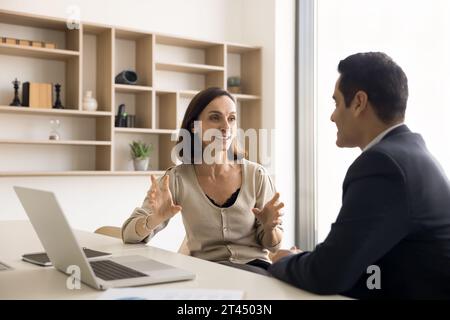 Positive, reife Geschäftsfrau, die mit einem indischen Kollegen spricht Stockfoto