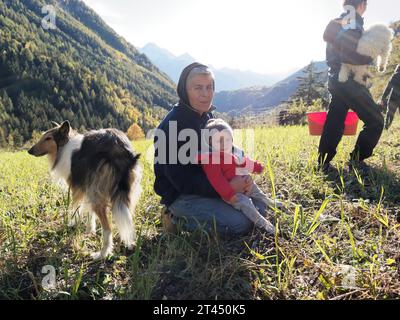 Großmutter hält während der Kartoffelernte einen Enkel neben einem Shetland Sheepdog auf einem Feld im Aostatal NW Italien. Oktober 2023 Stockfoto