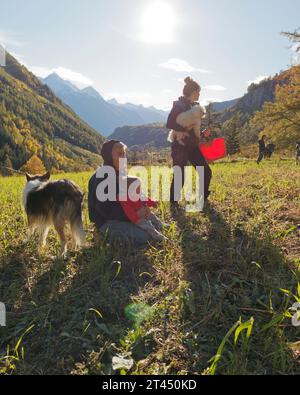 Großmutter hält während der Kartoffelernte einen Enkel neben einem Shetland Sheepdog auf einem Feld im Aostatal NW Italien. Oktober 2023 Stockfoto