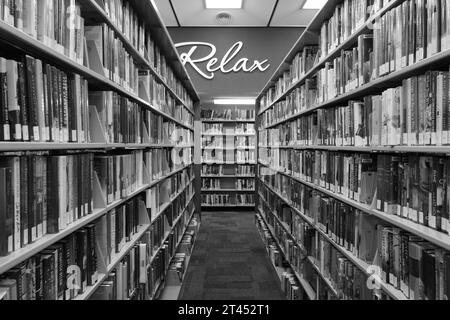 Bücher in Regalen in einer öffentlichen Bibliothek, mit einem „Relax“-Schild an der Wand Stockfoto