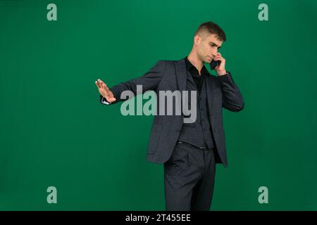 Verweigerungswelle Hand unzufriedener Gesichtsausdruck Lösen Sie das Problem STOP. Emotionen eines gutaussehenden Mannes auf grünem Hintergrund, Chromakey-Nahaufnahme, dunkles Haar, junger Mann. Telefon in Hand sprechen Stockfoto