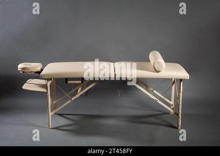 Tragbarer klappbarer Massagetisch für Physiotherapie-Behandlungsraum auf dunklem Hintergrund. Stockfoto