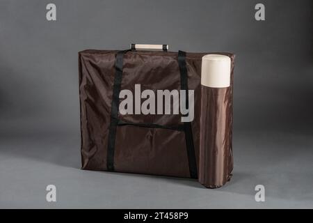 Tasche mit tragbarem klappbarem Massagetisch für Physiotherapie-Behandlungsraum auf dunklem Hintergrund. Stockfoto