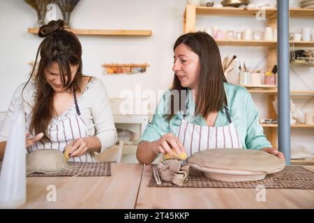 Zwei Frauen reden, während sie Tonbasteln im Töpferunterricht machen. Hobby- und Bastelkonzept. Stockfoto