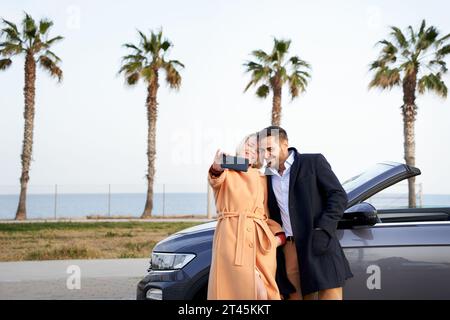 Ein Paar, das ein Smartphone benutzt, um ein Selfie außerhalb des Cabrios zu machen Stockfoto