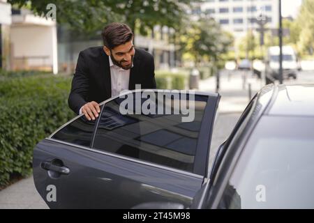 Ein lächelnder persönlicher Fahrer trifft sich und öffnet die Autotür für Lady Boss. Bodyguard-Aufgaben Stockfoto