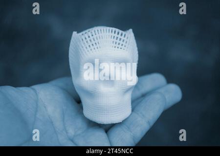 Person, die in der Handfläche einen kleinen Prototyp eines menschlichen Schädels in 3D hält, gedruckt aus geschmolzenem weißem Kunststoff. Dreidimensionales Modell. Additive progressive Medizintechnik. Moderne neue Druckindustrie. Stockfoto