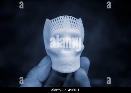 Person mit Fingern der Hand kleiner Prototyp eines menschlichen Schädels in 3D gedruckt aus geschmolzenem weißem Kunststoff. Dreidimensionales Modell. Additive progressive Medizintechnik. Moderne neue Druckindustrie. Stockfoto