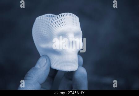 Person mit Fingern der Hand kleiner Prototyp eines menschlichen Schädels in 3D gedruckt aus geschmolzenem weißem Kunststoff. Dreidimensionales Modell. Additive progressive Medizintechnik. Moderne neue Druckindustrie. Stockfoto