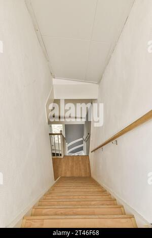 Einige Treppen führen zur Seite eines Gebäudes mit weißen Wänden und Holztreppen, die zu einem offenen Bereich im Zimmer führen Stockfoto