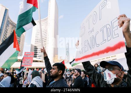 Toronto, Kanada - 28. Oktober 2023: Demonstranten halten palästinensische Fahnen und ein Schild mit der Aufschrift STOPPT DEN VÖLKERMORD in einer Stadt mit hohen Gebäuden Stockfoto