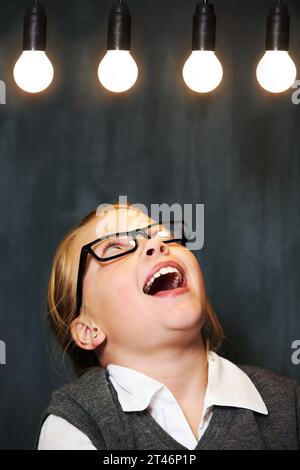 Glühbirnen, Lächeln und Kind mit Brille zum Denken, Ideen oder Brainstorming. Aufgeregt, lernend und glücklich Mädchen Kind mit positivem Stockfoto