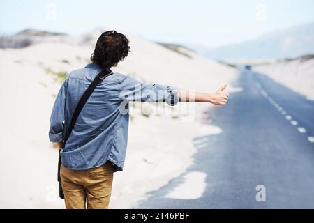 Zurück, Mann oder Anhalter in der Natur auf der Straße für Reise, Ziel oder Roadtrip mit Daumen nach oben auf der Straße. Rückansicht, Personen- oder Handbewegung im Freien oder Stockfoto