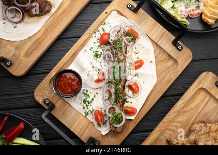Gegrillter Lula-Kebab auf Lavash mit Gemüse auf Holzbrett auf einem schwarzen Tisch Stockfoto