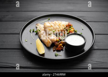 Gegrilltes Barsch-Fischfilet, serviert auf einem schwarzen Teller mit Gemüse und Sauce Stockfoto