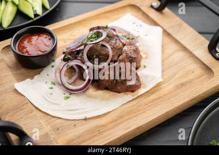 Schweinefleischstücke mit Zwiebeln auf Pitabrot. Mit Sauce auf Holzbrett servieren Stockfoto