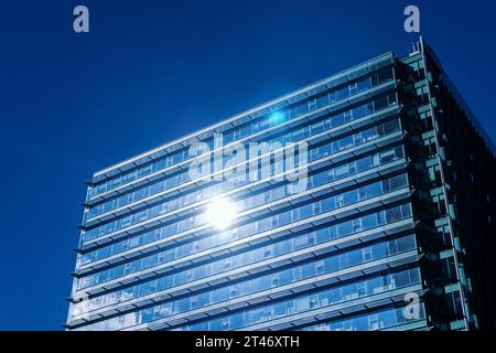 Das Sonnenlicht reflektiert in einem modernen Glashochhaus vor einem tiefblauen Himmel und betont die städtische Architektur. Stockfoto