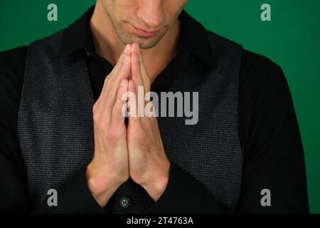 Emotionen eines gutaussehenden Mannes auf grünem Hintergrund, Chromakey-Nahaufnahme, dunkles Haar, junger Mann. Der Mann beugte sich vor Gott und betete zu Hause auf schwarzem Hintergrund. Hände im Gebet halten, Augen geschlossen. Stockfoto