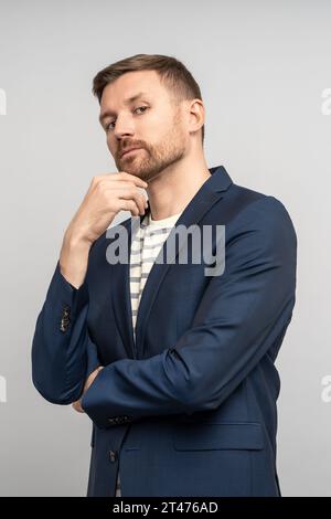 Selbstbewusster, entspannter, gutaussehender Mann mittleren Alters mit festem Look, der das Kinn berührt und in die Kamera blickt Stockfoto