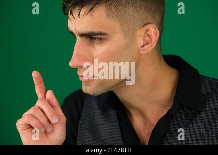 Junger glücklicher Geschäftsmann, der Daumen hoch geht, isoliert auf Grün Stockfoto