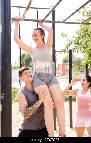 Gruppe junger männlicher und weiblicher Erwachsener, die Pull-Ups an der Bar machen. Drei Freunde trainieren im Freien und haben eine gute Zeit. Stockfoto