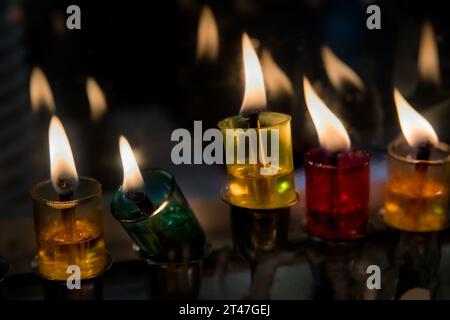 Mehrfarbige Glasfläschchen halten Öl und brennende Dochte in einer Menora, die während des jüdischen Festivals von Hanukka hell leuchtet. Stockfoto