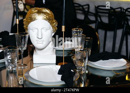 Üppige Tischgestaltung bei einer Hochzeit oder gehobenen Veranstaltung mit exquisitem Geschirr. Eine Marmorskulptur einer goldhaarigen Frau und opulenten schwarzen... Stockfoto