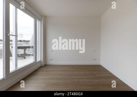 Panoramablick auf ein Wohnzimmer mit Holzfußboden und Zugang zur Terrasse in einem Apartment durch eine Glastrennwand Stockfoto