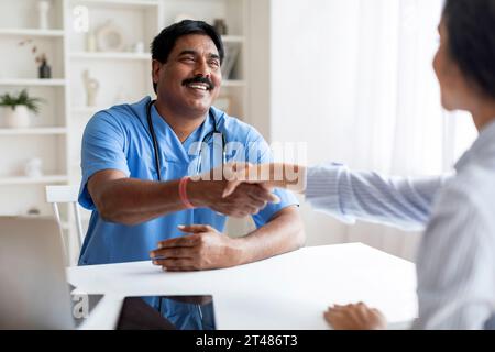 Lächelnder Indischer Arzt In Uniform, Der Mit Weiblicher Patientin Die Hände Schüttelt Stockfoto