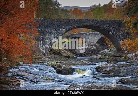 Invermoriston, Highlands, Schottland, Großbritannien. Oktober 2023. Trocken, bewölkt und kühl bei 8 Grad Celsius mit beißendem Wind E 19 km/h mit möglichen Böen von 30 km/h. Im Bild: Die Invermoriston Bridge und Telford Bridge hinter dem Fluss Moriston umgeben von herbstlichem Laub. Quelle: Archwhite/Alamy Live News. Stockfoto