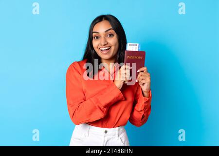 Glückliche indische Reiserin zeigt Bordkarte in blauem Studio Stockfoto