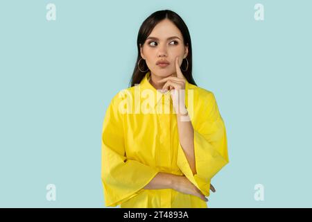 Eine verdächtige junge Frau, die beiseite blickt und ihr Gesicht berührt Stockfoto
