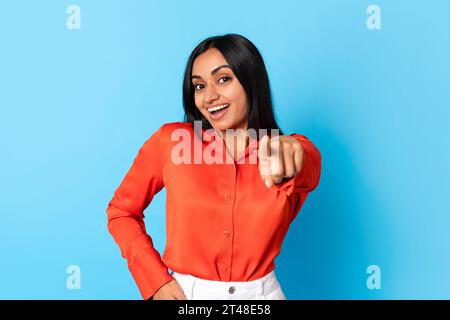 Lächelnde hindu-Dame vor blauem Hintergrund, die mit dem Finger auf die Kamera zeigt Stockfoto