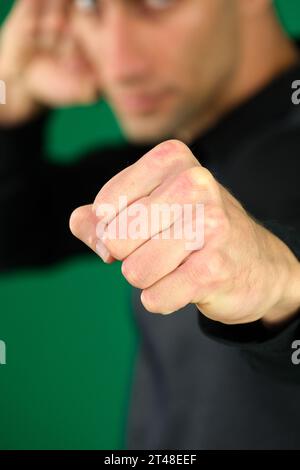 Emotionen eines gutaussehenden Mannes auf grünem Hintergrund Chromakey Nahaufnahme dunkles Haar junger Mann Porträt eines bärtigen Mannes, der mit Boxfäusten steht und bereit ist anzugreifen oder sich zu verteidigen, mit wütendem Gesicht schaut, Stockfoto