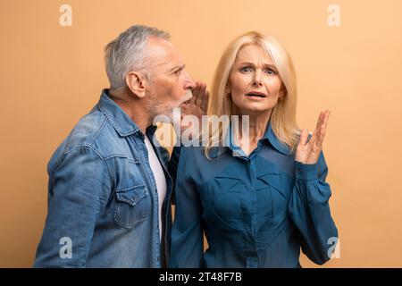 Älterer Mann, der sein Geheimnis mit seiner Frau teilt, beiger Hintergrund Stockfoto