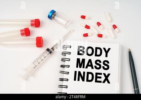 Medizinisches Konzept. Auf dem Tisch befinden sich Pillen, Injektionen, eine Spritze und ein Notizblock mit der Aufschrift „BODY MASS INDEX“ Stockfoto