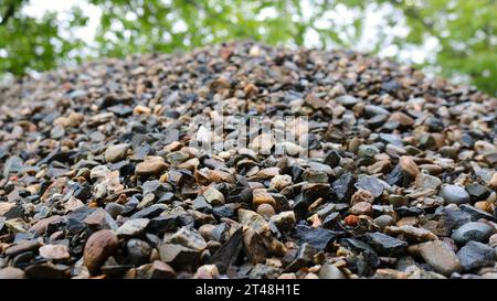 Ein Haufen grauer Kies, von unten nach oben sichtbar, auf der Straße unter einem Baum gelegen, natürliche Textur aus Stein, zerquetschtem Mineral Stockfoto