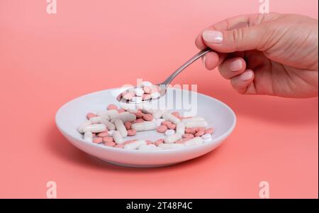 Frau Hand nimmt Löffel von Gewichtsverlust Pillen von Platte mit vielen rosa und weißen Tabletten und Kapseln auf rosa Hintergrund. Medizinische Behandlung, weiblich Stockfoto