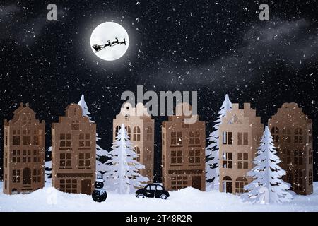 Winterdorf aus Papier. Papier Winter Stadt Nacht Landschaft mit Santa-Klausel Schlitten über Vollmond. Kreative Weihnachtskomposition mit Papierho Stockfoto