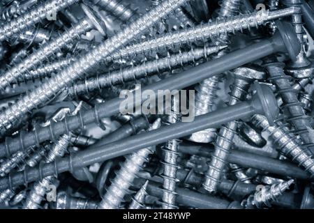 Viele Schrauben liegen flach auf abstraktem Hintergrund in blauem Ton Stockfoto