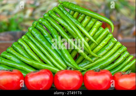 Grüne Chilischoten ordentlich in dreieckiger Form angeordnet mit Tomaten nebeneinander an der Basis Stockfoto