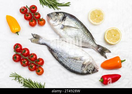 Frischer dorado-Fisch mit Gemüse. Rote Tomaten, farbige Paprika, grüner Rosmarin, Zitrone auf weißem Hintergrund. Flache Lagen Stockfoto