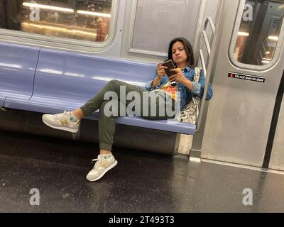 Am Mittwoch, 25. Oktober 2023, loungert abgelenkte Frau auf dem Sitz in der New Yorker U-Bahn. (© Frances M. Roberts) Stockfoto