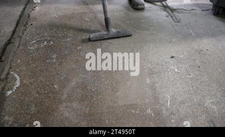 Ein Arbeiter auf einer Baustelle reinigt den Betonboden nach der Arbeit mit einem Staubsauger von Staub. Vorbereitung des Regiments auf Reparaturen. A Stockfoto