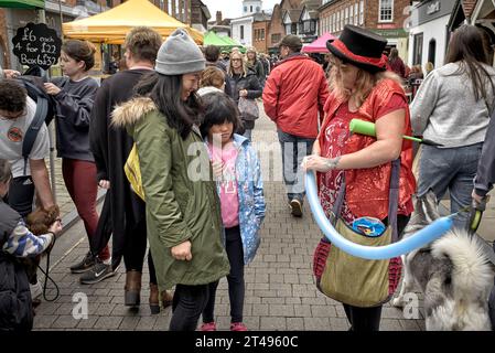 Weibliche Straßenunterhalterin formt einen Ballon für eine asiatische Mutter und ein Kind. England Großbritannien Stockfoto